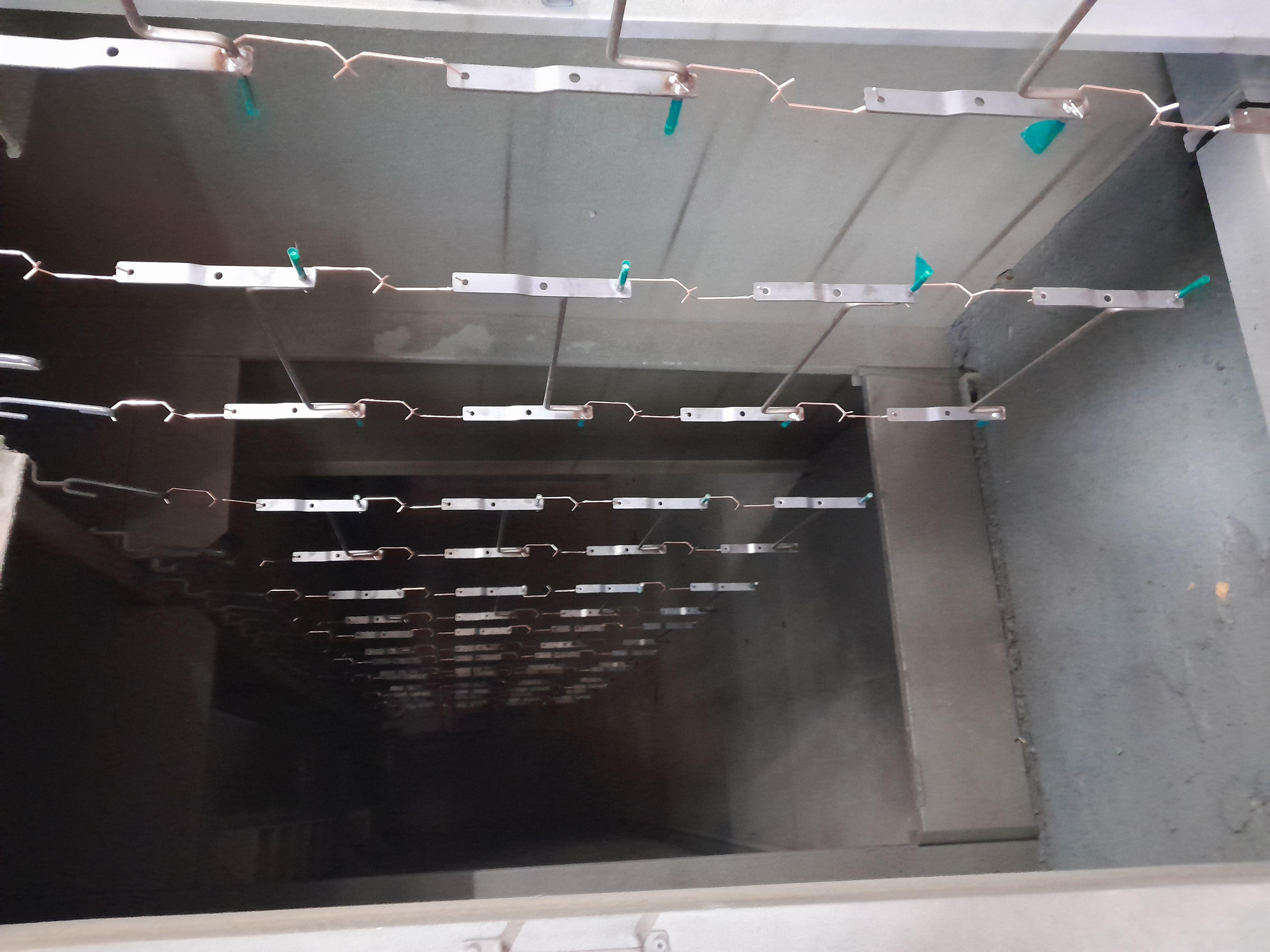 Metal brackets suspended on hanging racks inside an industrial powder coating oven tunnel with teal plastic hooks