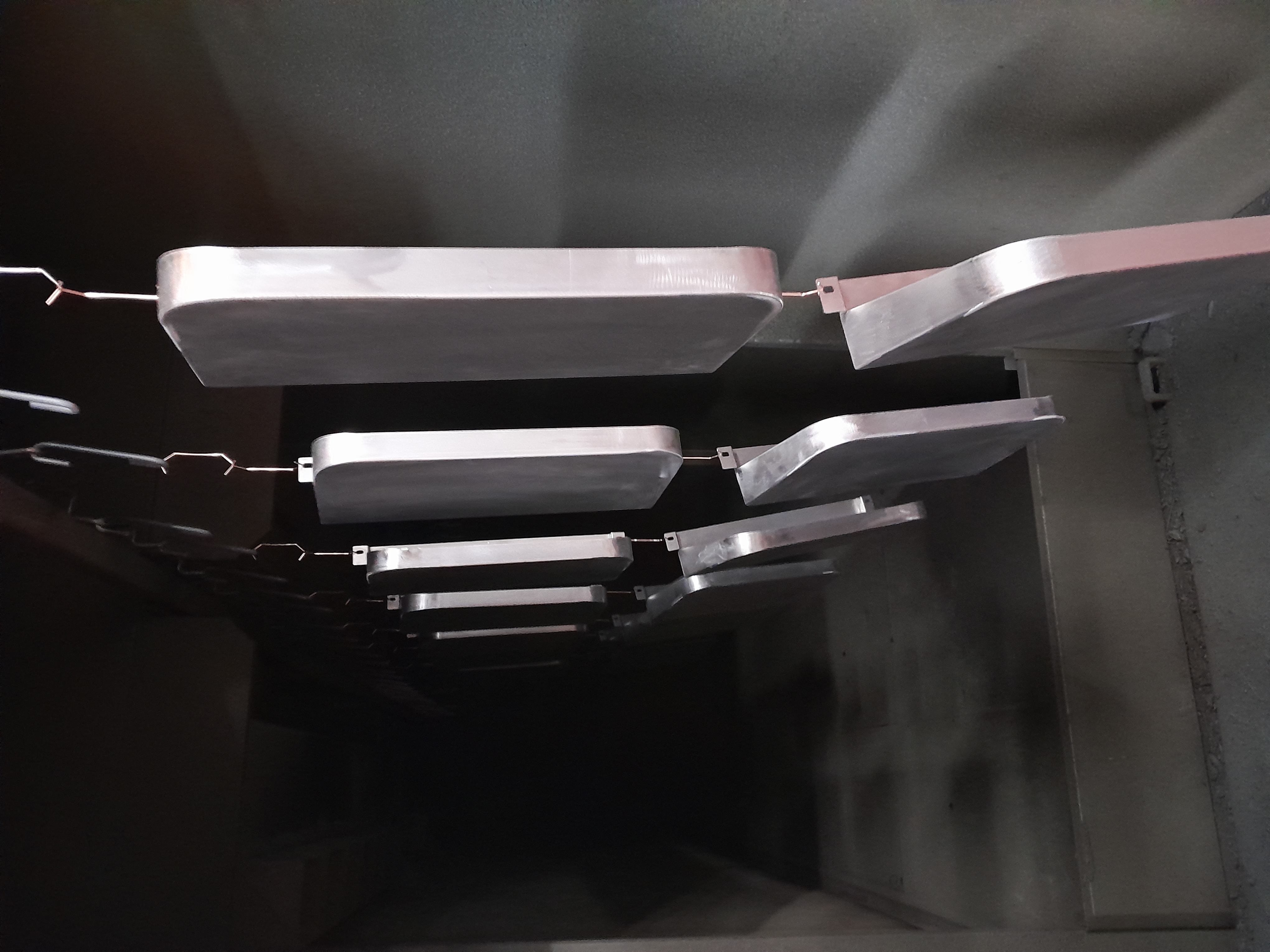 Metal components hanging from hooks inside a dark plastic coating oven tunnel, receding into the distance