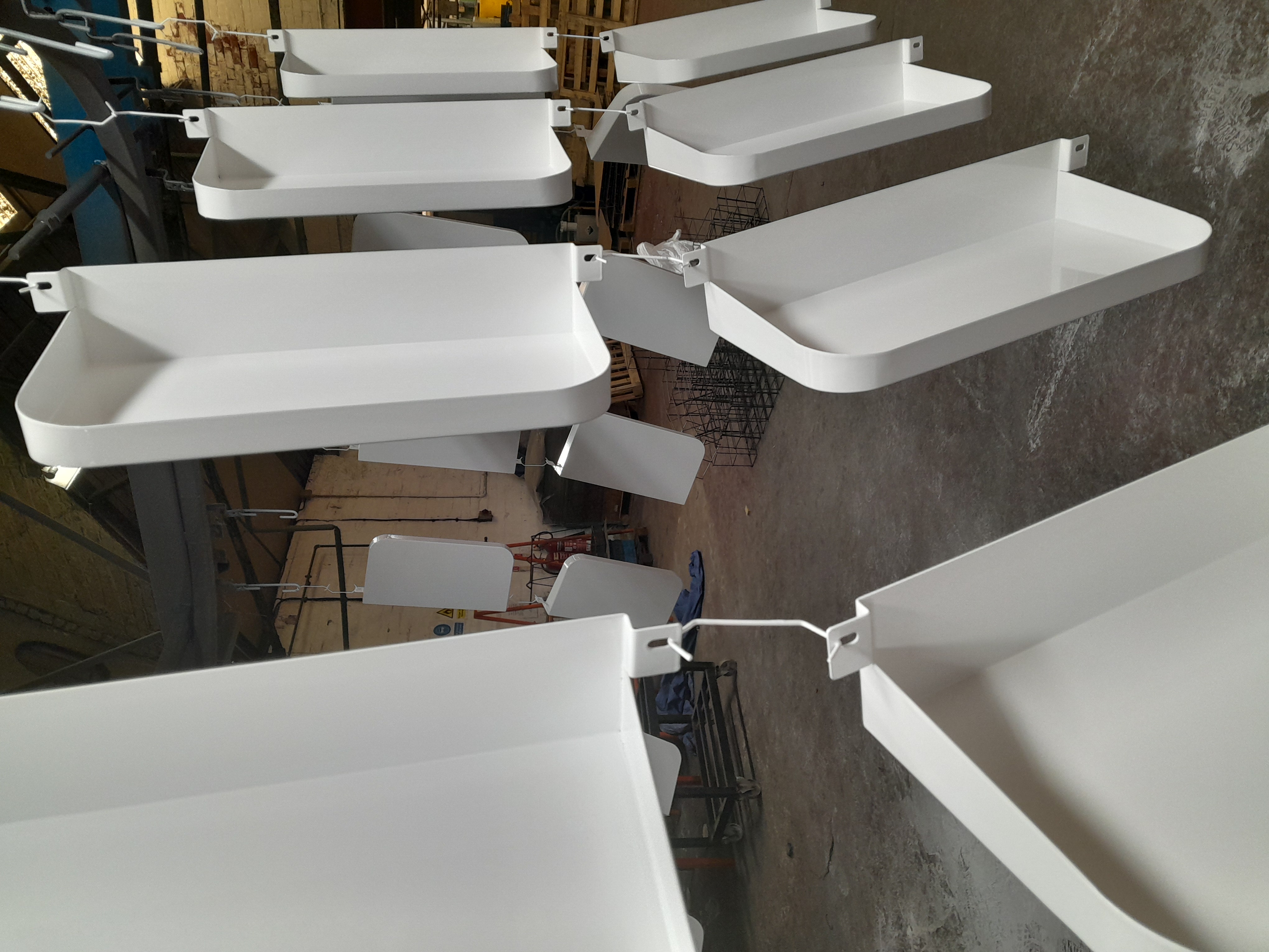 White powder-coated metal components hanging from hooks on a conveyor line inside an industrial factory unit