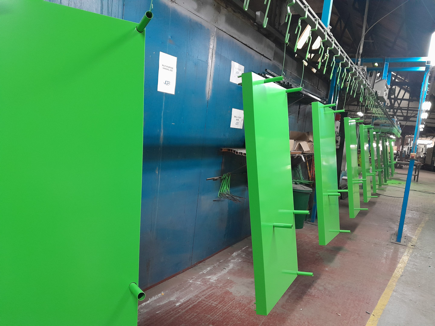 Row of bright green powder-coated metal fabrications lined up inside an industrial manufacturing facility