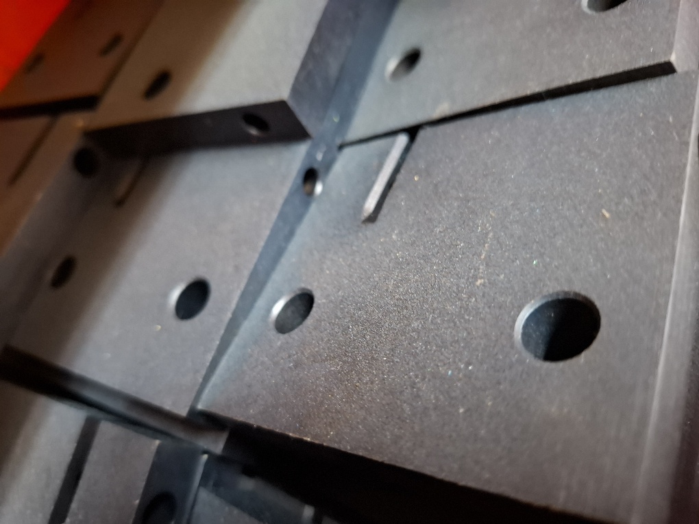 Close-up of blackodised machined steel plates with precision-cut slots and drilled holes stacked in a workshop