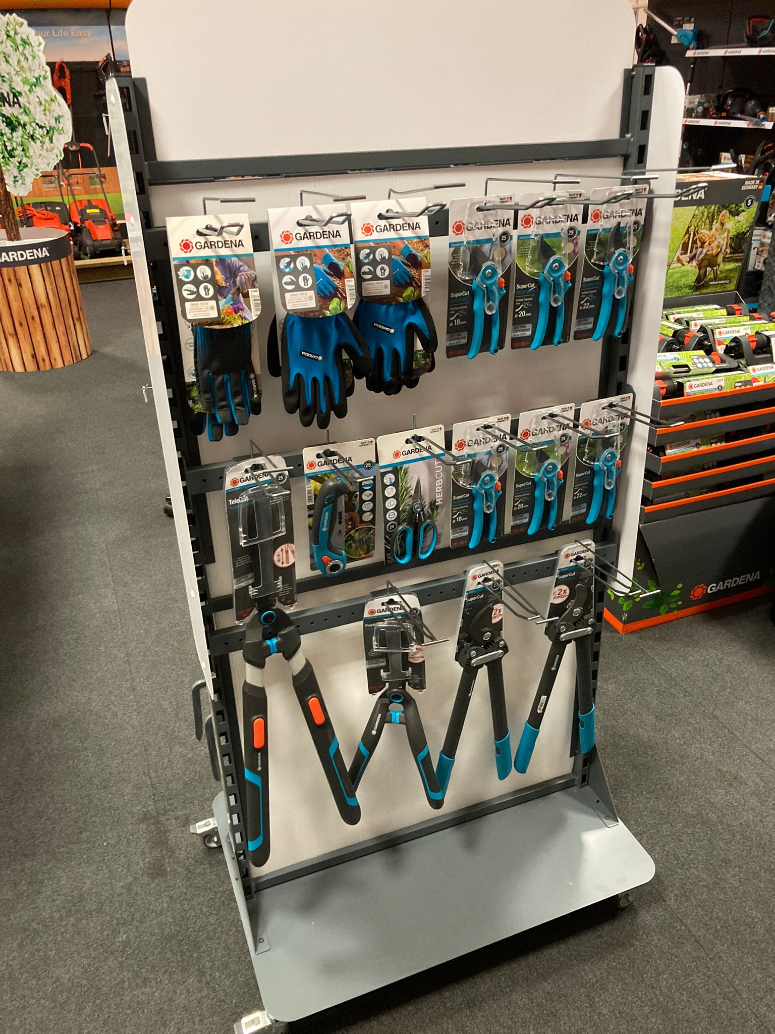 Gardena branded retail display stand featuring gardening gloves, secateurs, loppers and herb scissors in a garden centre store