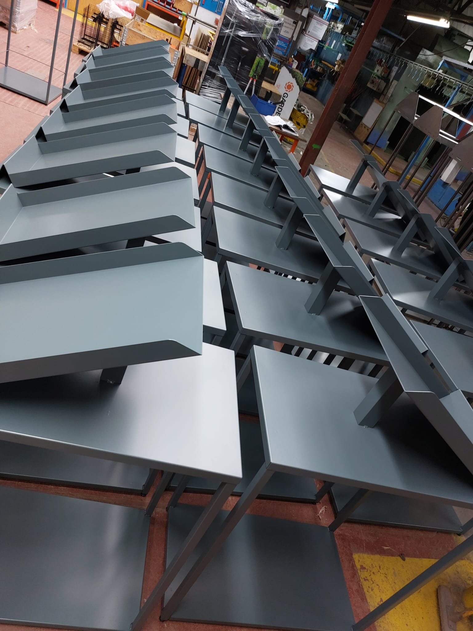 Rows of grey powder-coated sheet metal tables and shelving units lined up inside a manufacturing workshop