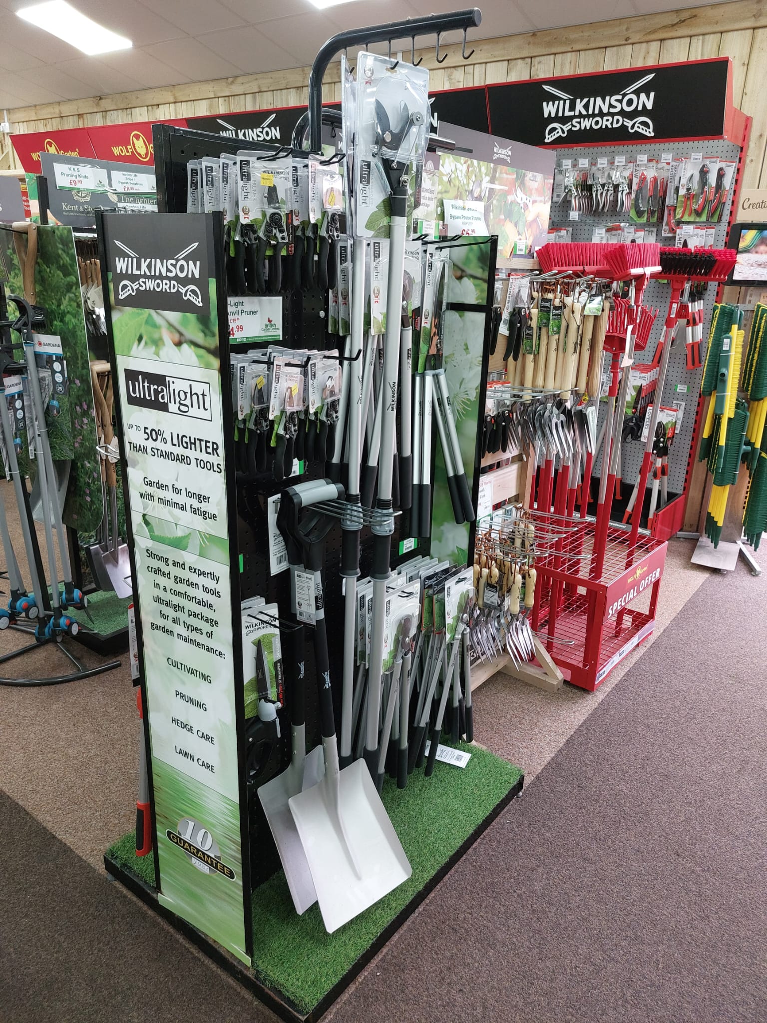 Wilkinson Sword Ultralight garden tools aisle display in a garden centre, featuring pruners, loppers and spades on a freestanding stand.