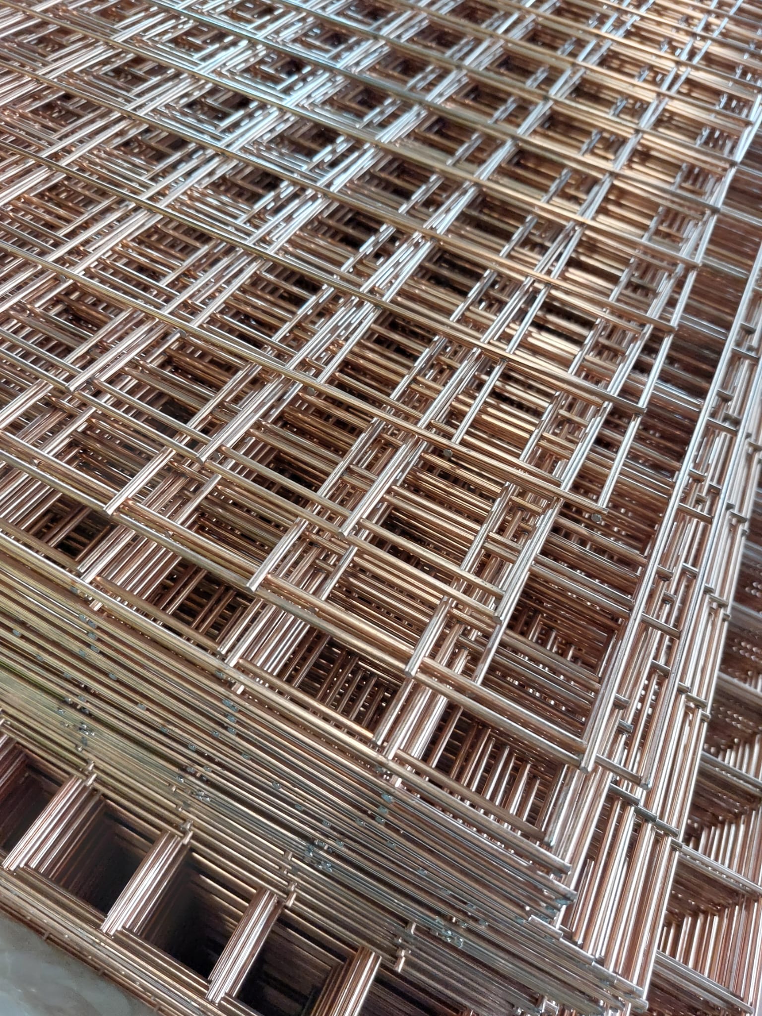 Stacked panels of bespoke wire mesh with a copper-toned welded grid pattern, viewed at a close angle