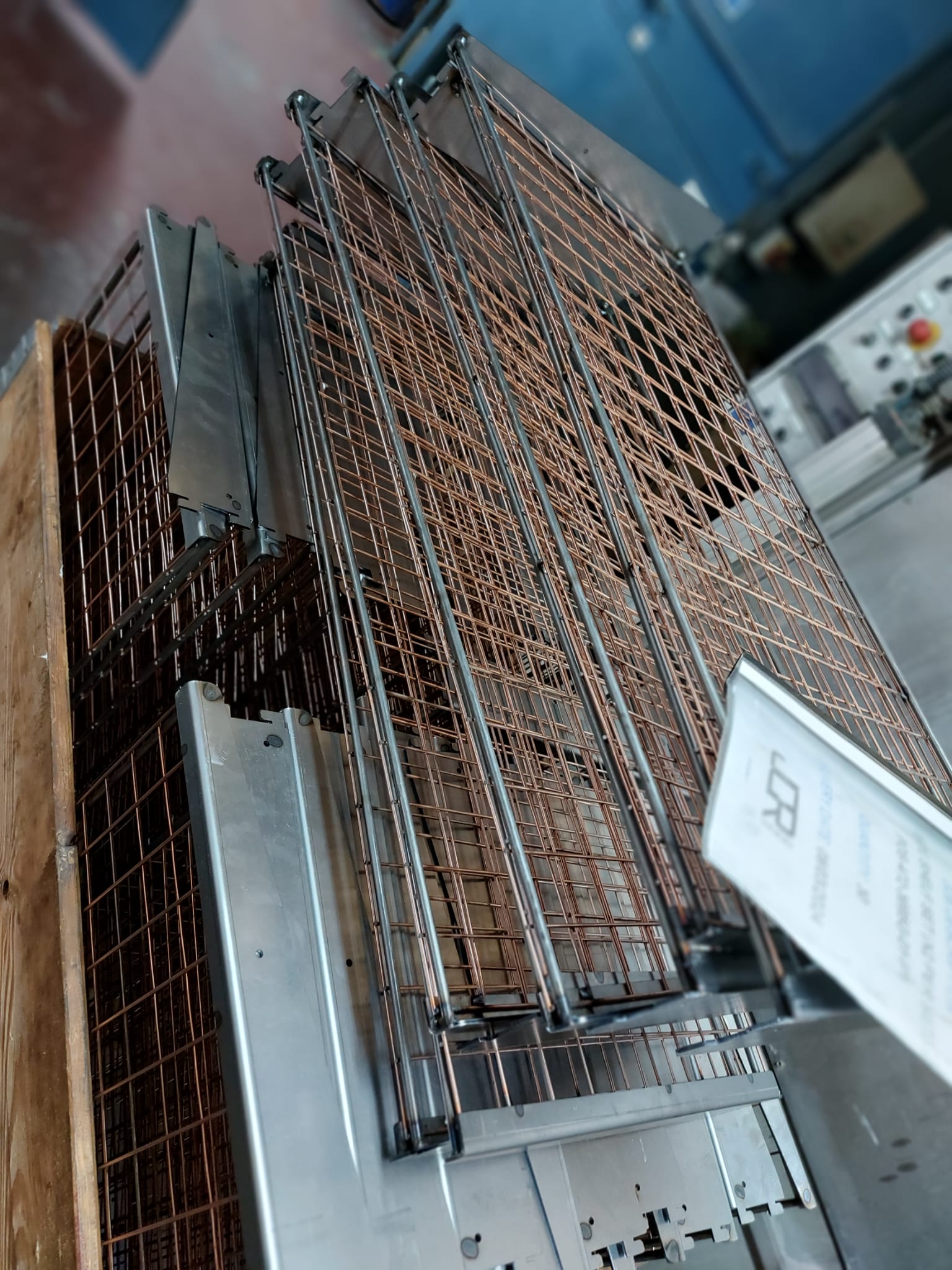 Stacked bespoke wire work panels with copper mesh grids and steel frames stored in an industrial workshop setting