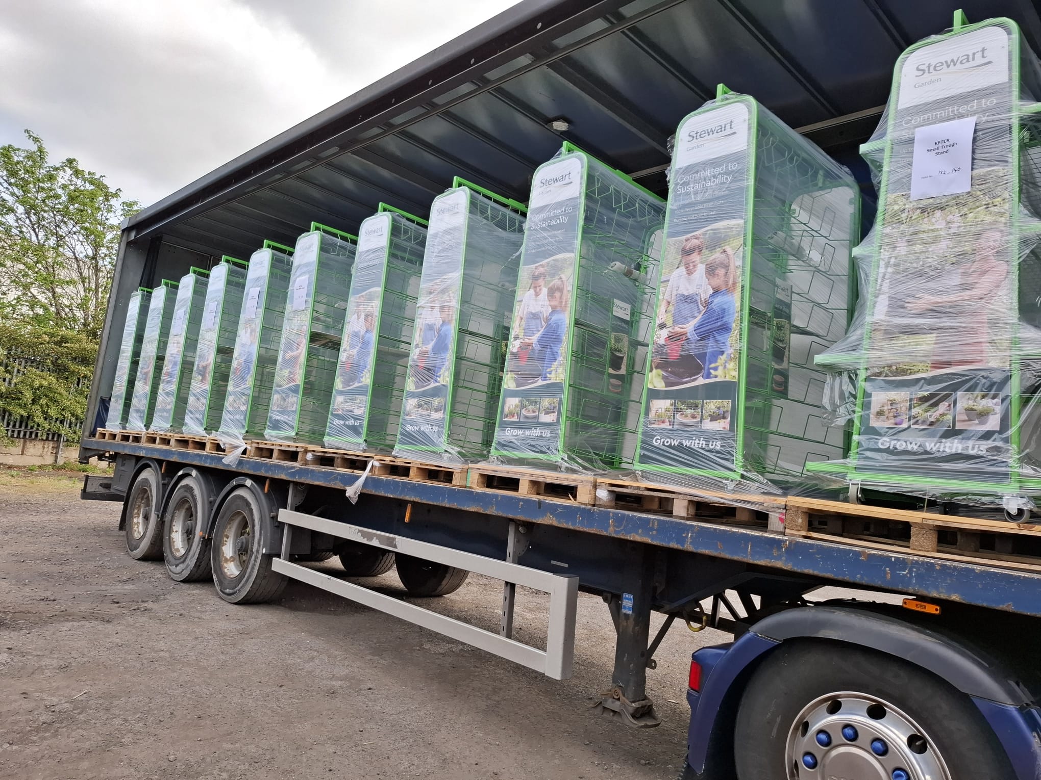 A flatbed lorry loaded with pallets of shrink-wrapped Stewart Garden metal display stands ready for delivery