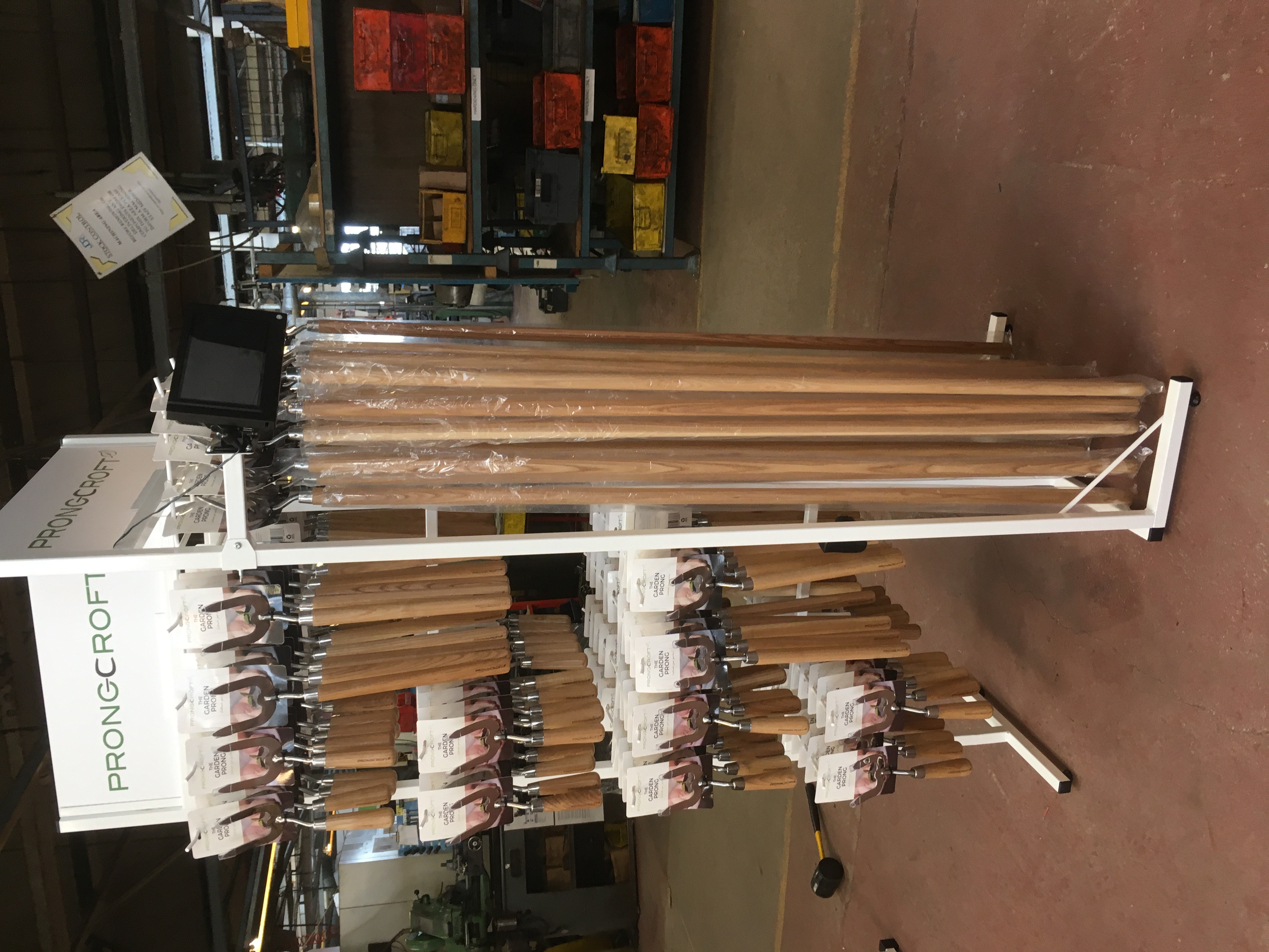Prongcroft branded aisle display stand holding packaged garden prong hand tools with wooden handles in a warehouse setting
