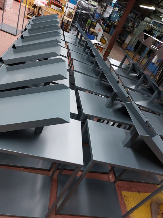 Rows of grey powder-coated sheet metal tables and shelving units lined up inside a manufacturing workshop