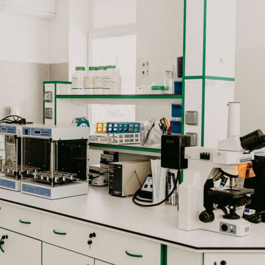 White bespoke laboratory furniture with green trim, supporting a microscope, sample incubators, reagent bottles, and test tube racks