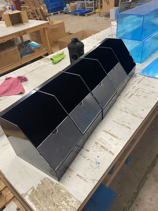 Black acrylic counter top display unit with multiple open compartments, sitting on a workbench in a manufacturing workshop.