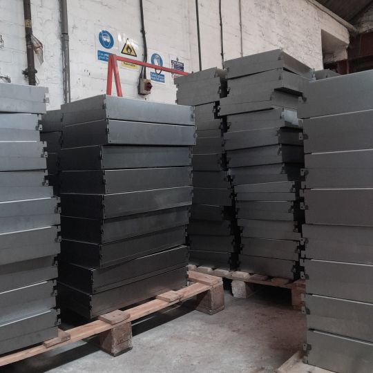 Stacks of fabricated sheet metal components piled on wooden pallets inside an industrial workshop