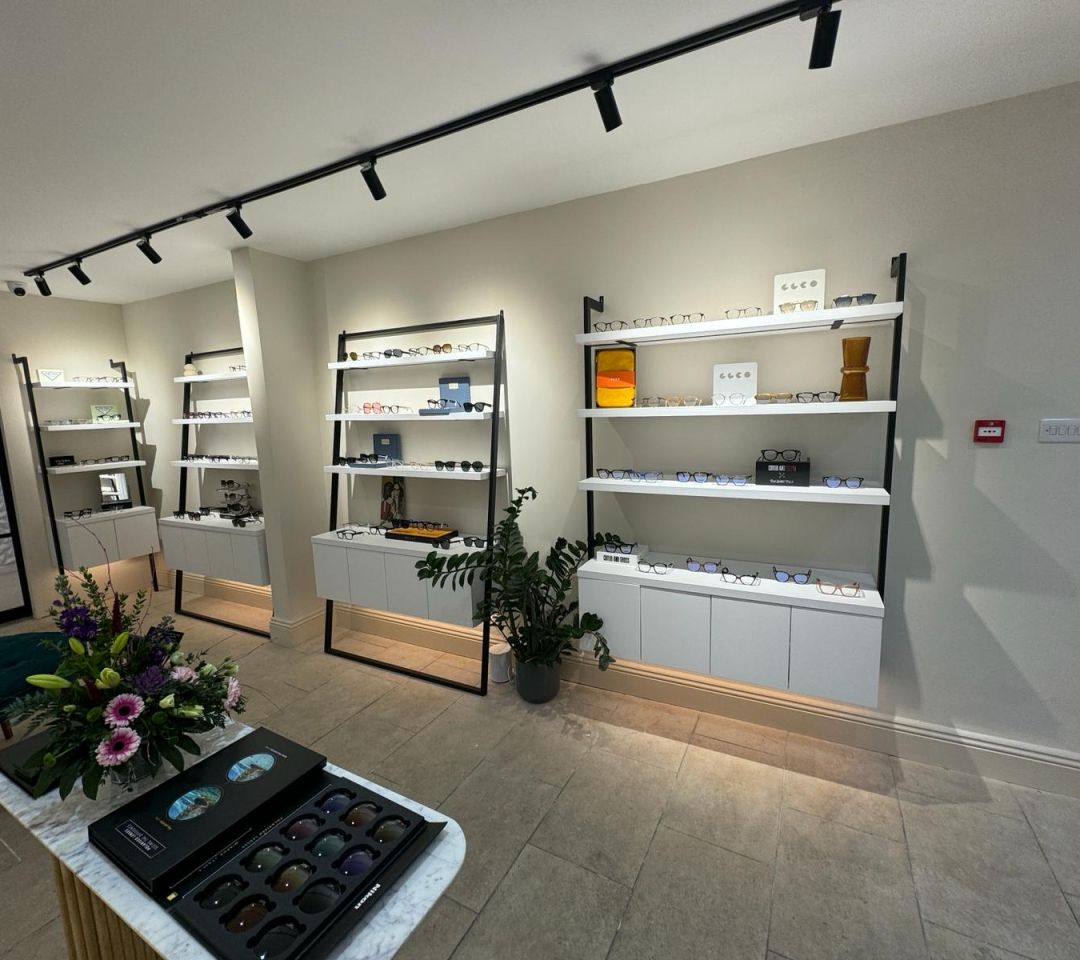 Modern optician showroom interior with glasses displayed on white wall-mounted shelving units under black track lighting