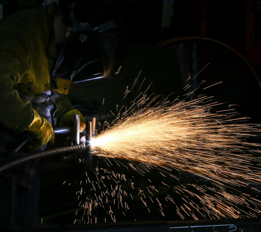 Welder in a protective mask and gloves welding metal, sending a bright spray of sparks across a dark workshop