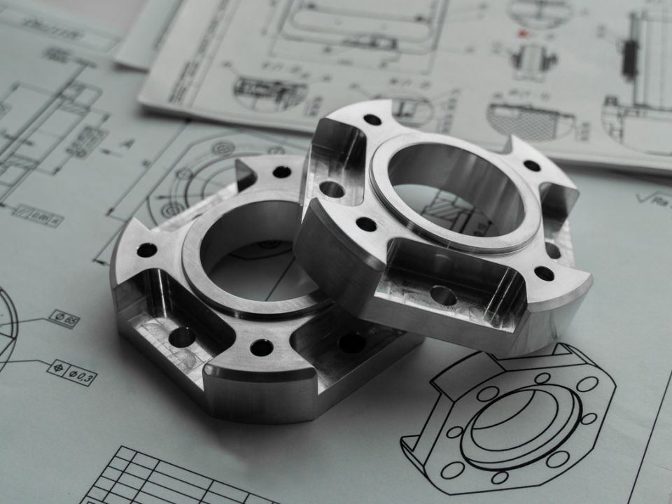 Two precision-machined metal flanged components resting on detailed engineering technical drawings