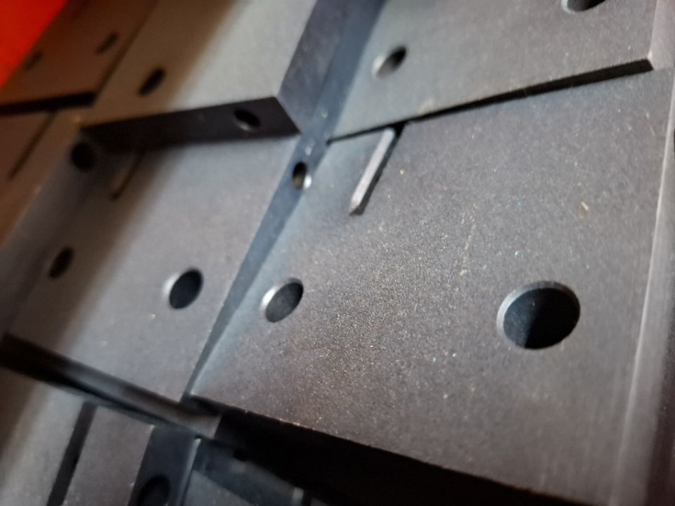 Close-up of blackodised machined steel plates with precision-cut slots and drilled holes stacked in a workshop
