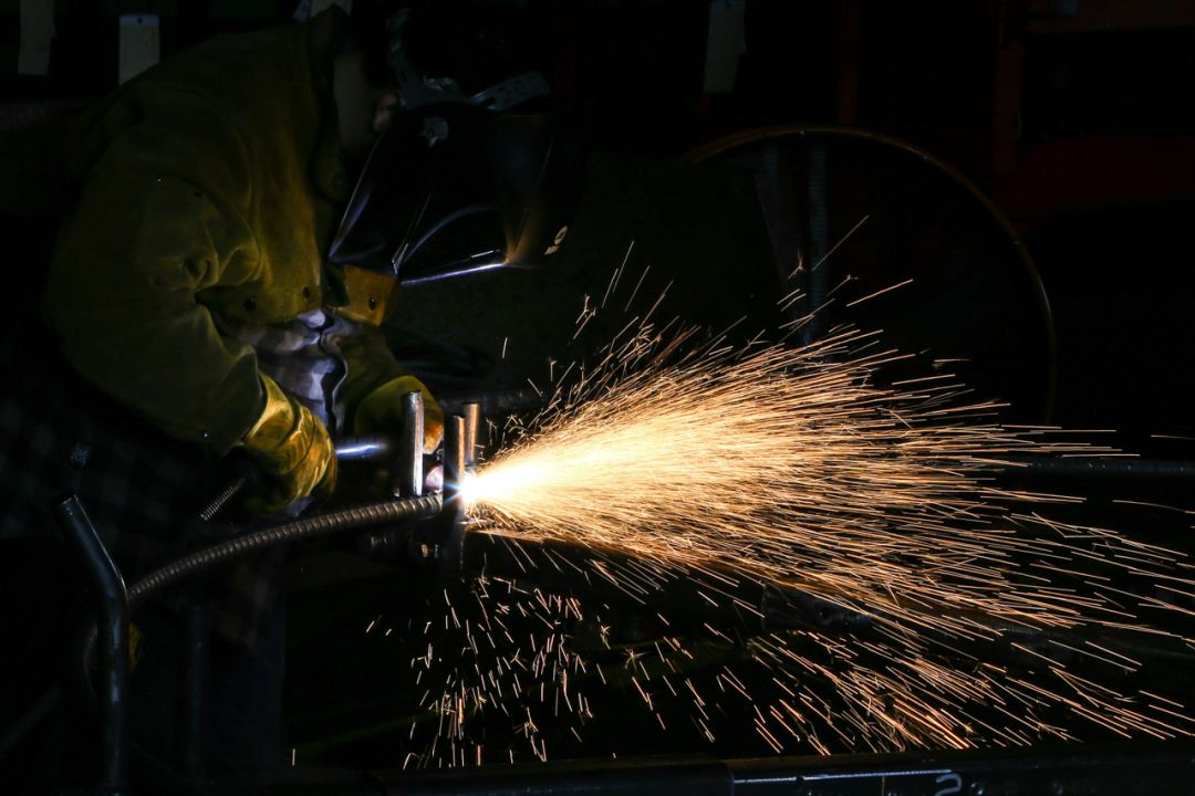 Welder in a protective mask and gloves welding metal, sending a bright spray of sparks across a dark workshop