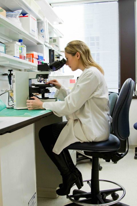 Female scientist in a white lab coat examining a sample through a microscope at a bespoke laboratory furniture workbench