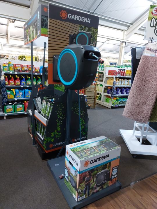 Gardena wall-mounted hose box display unit in a garden centre aisle with branded product boxes and accessories on show