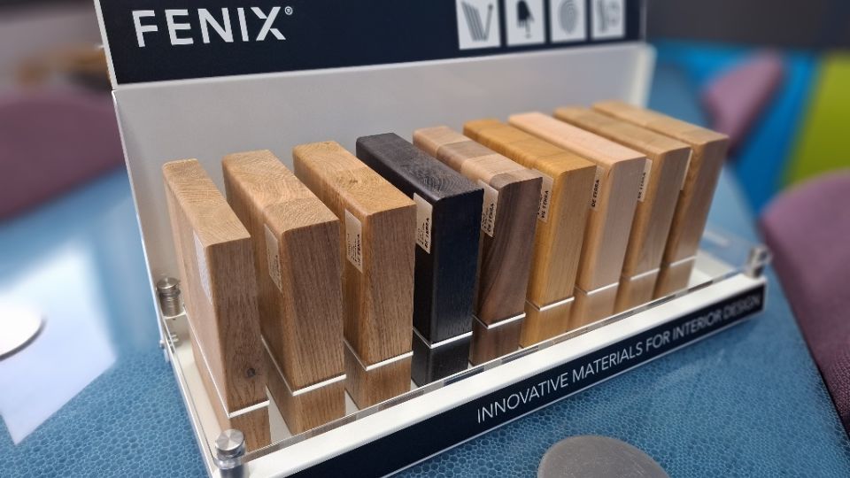 Fenix branded countertop display stand holding wood-effect material samples in various tones for interior design
