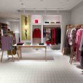 Bright clothing boutique interior with wooden rails, folded garments on a display table, and colourful jackets hung on a white tiled wall