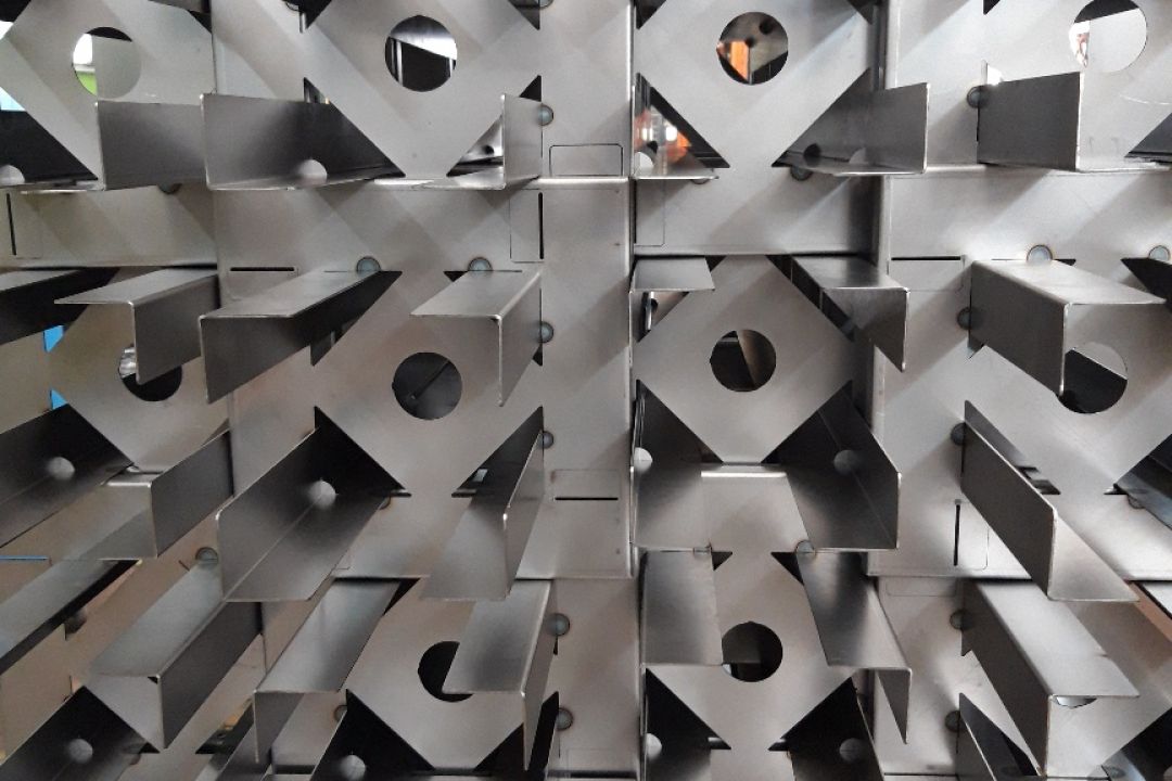 Stacks of fabricated sheet metal components on wooden pallets inside a workshop with safety signs on the wall