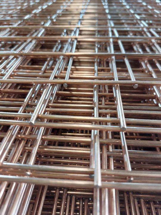 Close-up of stacked stainless steel welded wire mesh panels with square grid pattern, showing copper-toned metallic sheen