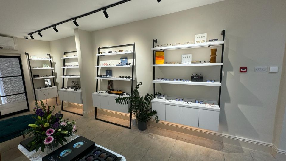 Modern optician showroom interior with glasses displayed on white wall-mounted shelving units under track lighting