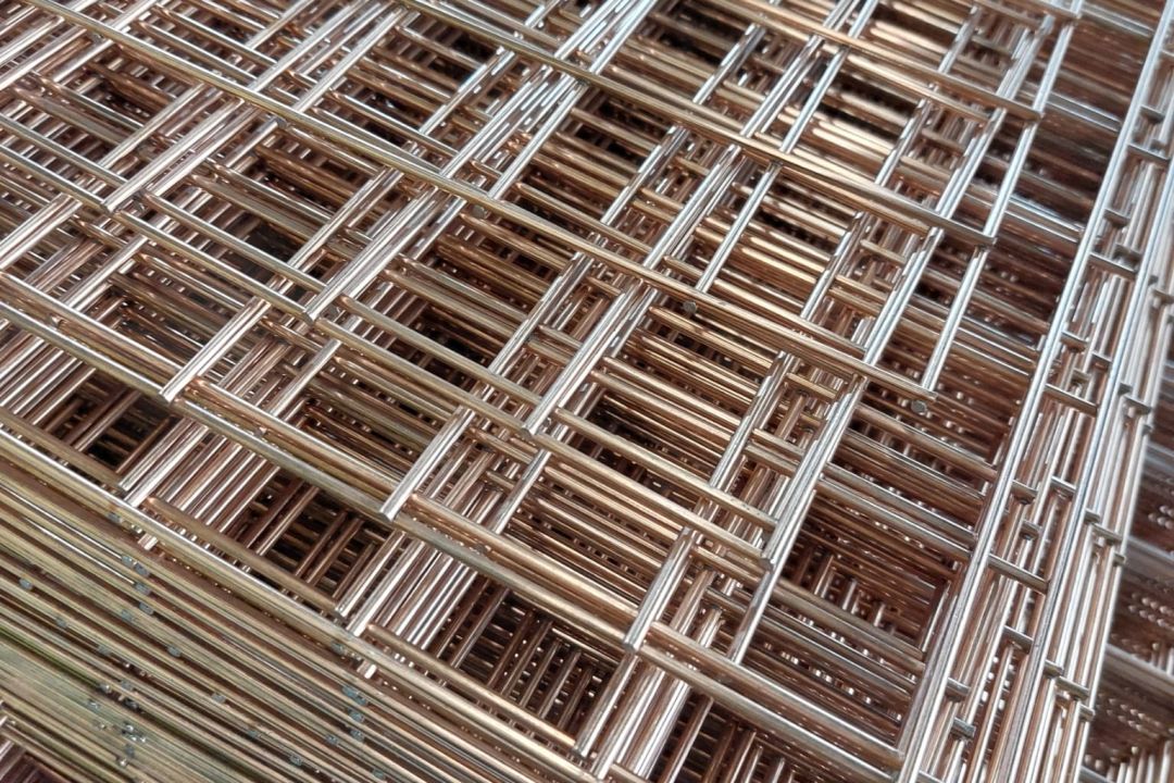 Stacked panels of bespoke wire mesh with a copper-toned welded grid pattern, viewed at a close angle