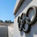 Close-up of a weathered metal Olympic rings emblem mounted on a white stone wall at an empty stadium
