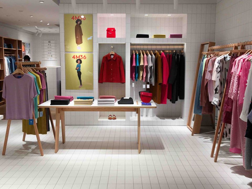 Bright clothing boutique interior with wooden rails, folded garments on a display table, and colourful jackets hung on a white tiled wall