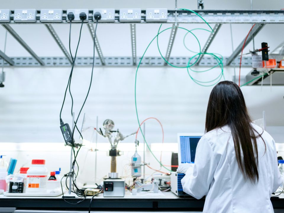 Female scientist in a white lab coat working at a bench fitted with bespoke laboratory furniture, cables, and equipment