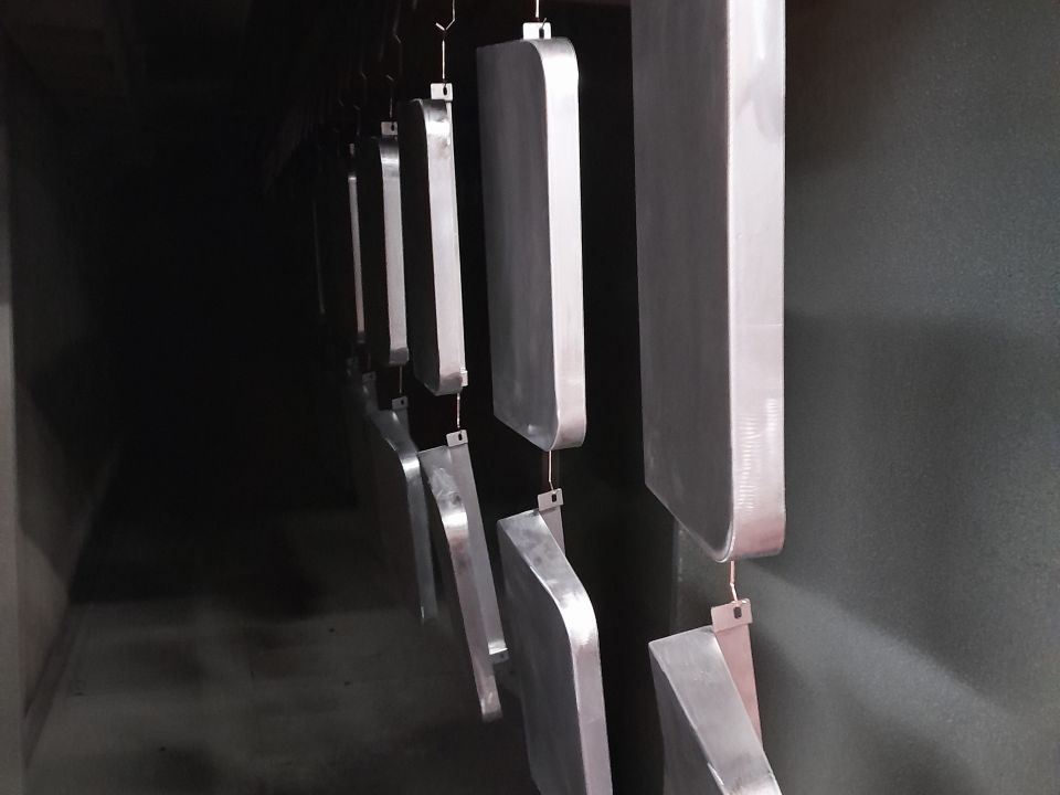 Metal components hanging from hooks inside a dark plastic coating oven tunnel, receding into the distance