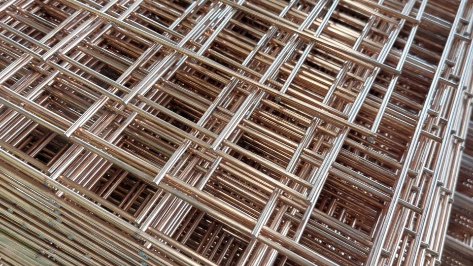 Stacked panels of bespoke wire mesh with a copper and silver welded grid pattern, photographed at an angle