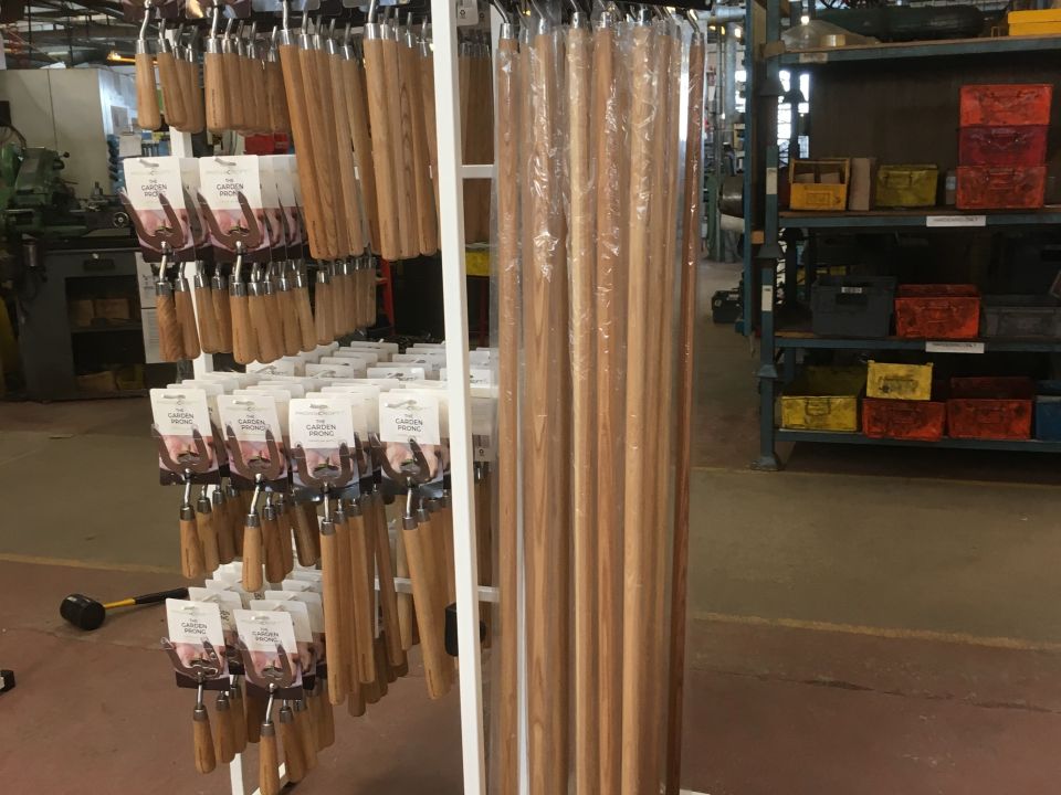Prongcroft branded aisle display stand holding packaged garden prong hand tools with wooden handles in a warehouse setting
