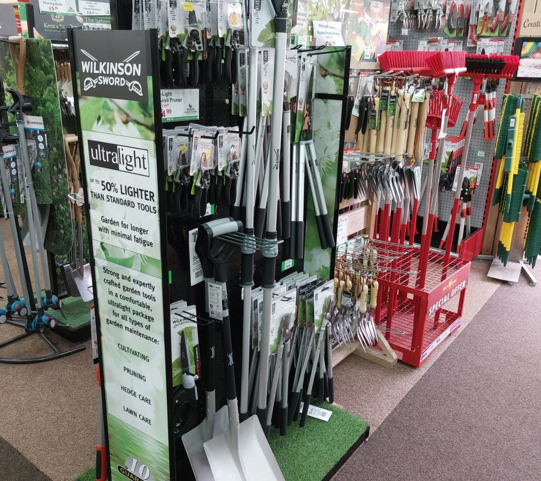 Wilkinson Sword Ultralight garden tools aisle display in a garden centre, featuring pruners, loppers and spades on a freestanding stand.