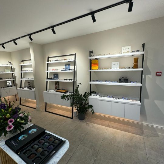 Modern optician showroom interior with glasses displayed on white wall-mounted shelving units under track lighting