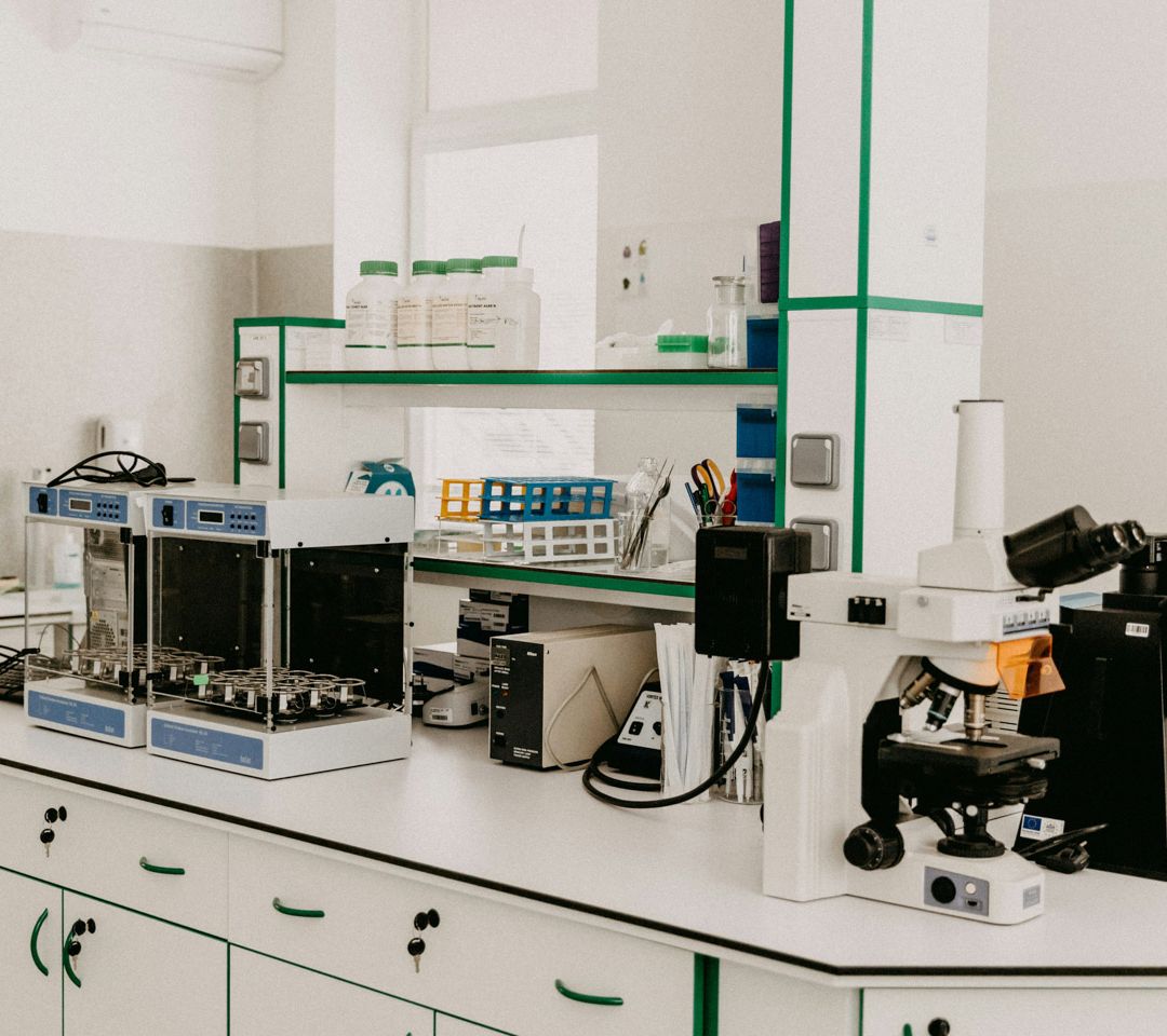 White bespoke laboratory furniture with green trim, fitted with a microscope, sample incubator, reagent bottles, and test tube racks