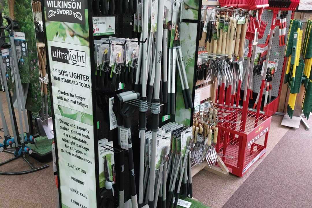 Wilkinson Sword Ultralight garden tools aisle display in a garden centre, featuring pruners, loppers and spades on a freestanding stand.