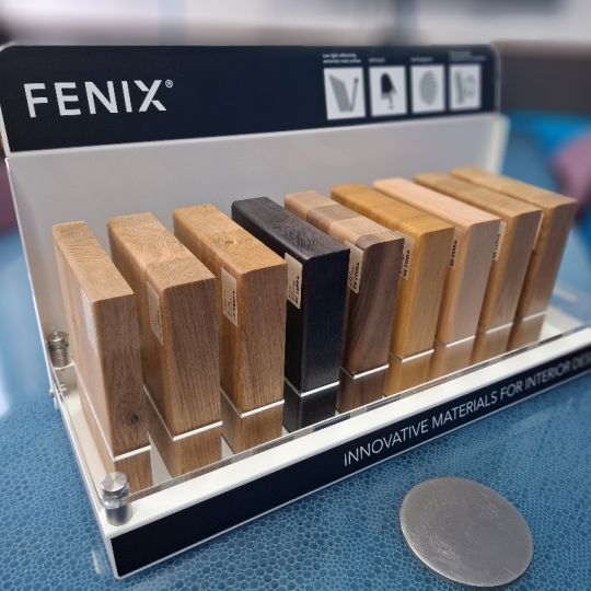 Fenix branded countertop display stand holding wood-effect material samples in various tones for interior design