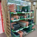 Stewart Garden trough shop display stand stacked with terracotta, green, and grey plastic troughs and planters in a garden centre