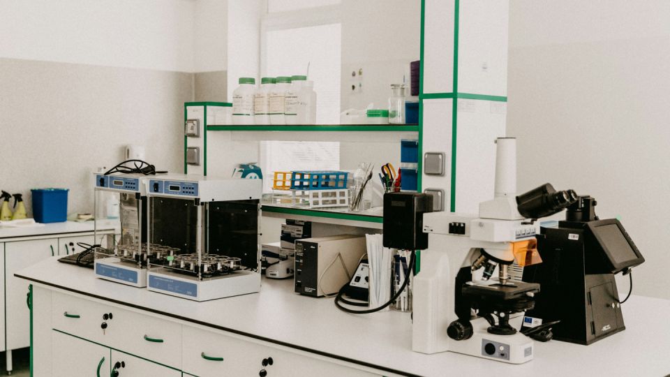 White bespoke laboratory furniture with green trim, supporting a microscope, sample incubators, reagent bottles, and test tube racks