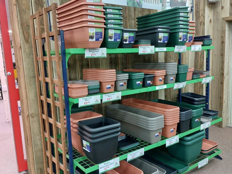 Stewart Garden trough shop display stand stacked with terracotta, green, and grey plastic troughs and planters in a garden centre