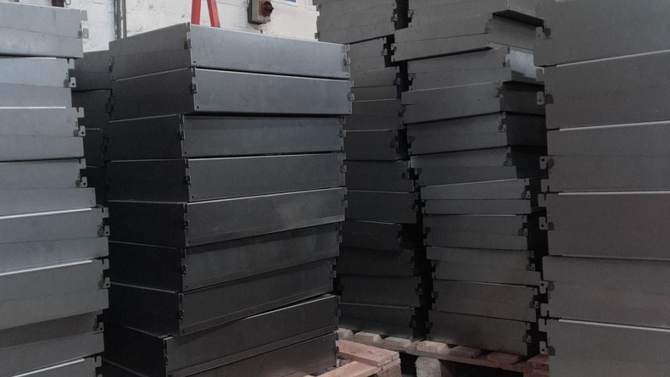 Stacks of fabricated sheet metal components piled on wooden pallets inside an industrial workshop